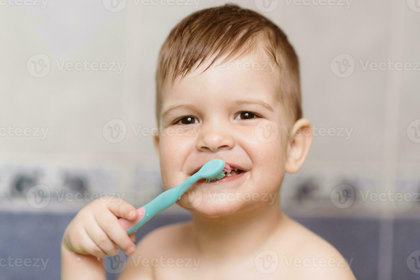 bello bambino spazzolatura il suo denti con un' spazzolino nel il bagno foto