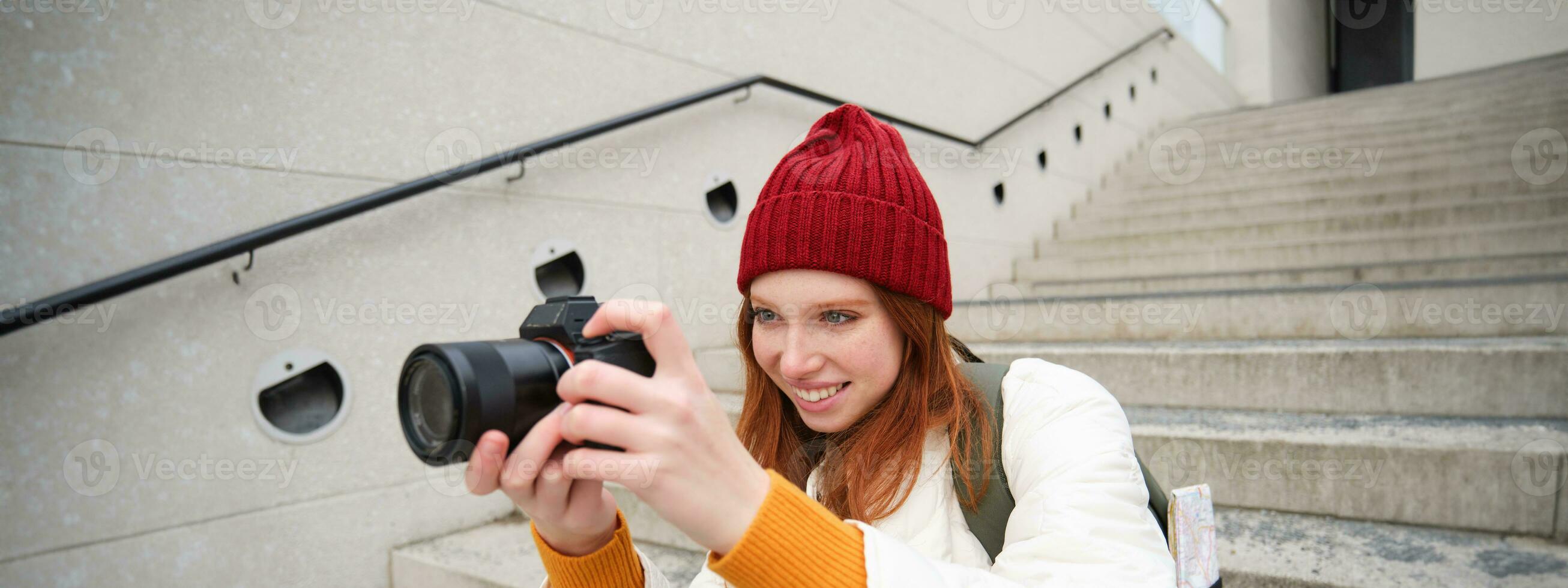 urbano persone e stile di vita. contento testa Rossa donna prende fotografie, Tenere professionale digitale telecamera, Fotografare su strade foto