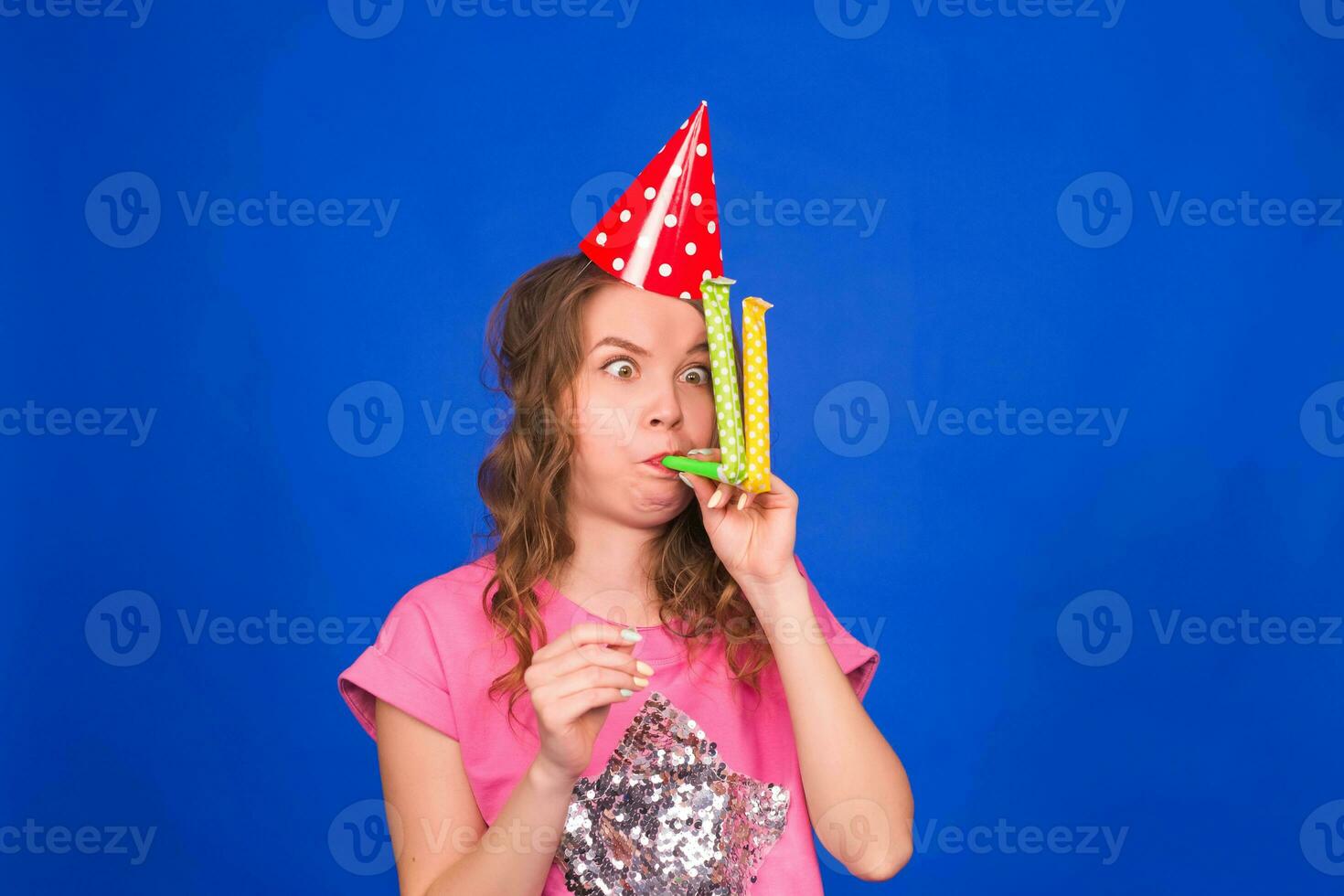 divertente giovane donna nel un' compleanno berretto soffiaggio un' fischio su un' blu sfondo foto
