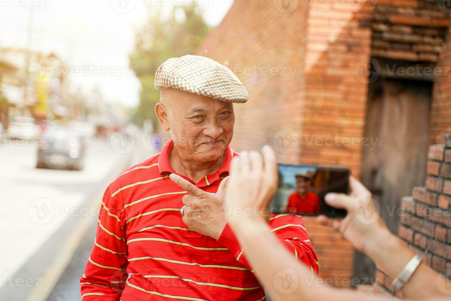 avvicinamento anziano Cinese turista pose per il suo amico per prendere fotografie mentre a piedi in giro il città su sole bagliore e sfocato di città sfondo.