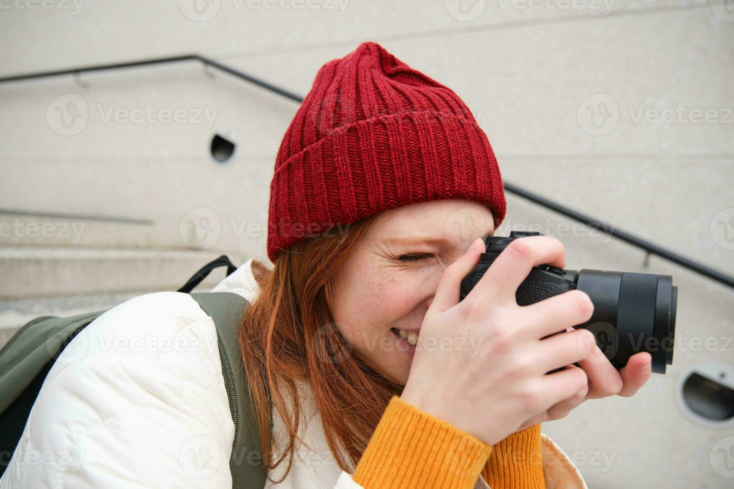 urbano persone e stile di vita. contento testa Rossa donna prende fotografie, Tenere professionale digitale telecamera, Fotografare su strade foto