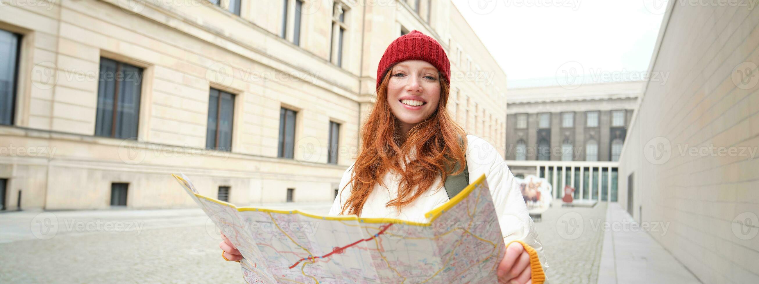 bellissimo testa Rossa donna, turista con città carta geografica, esplora giro turistico storico punto di riferimento, a piedi in giro vecchio cittadina, sorridente felicemente foto