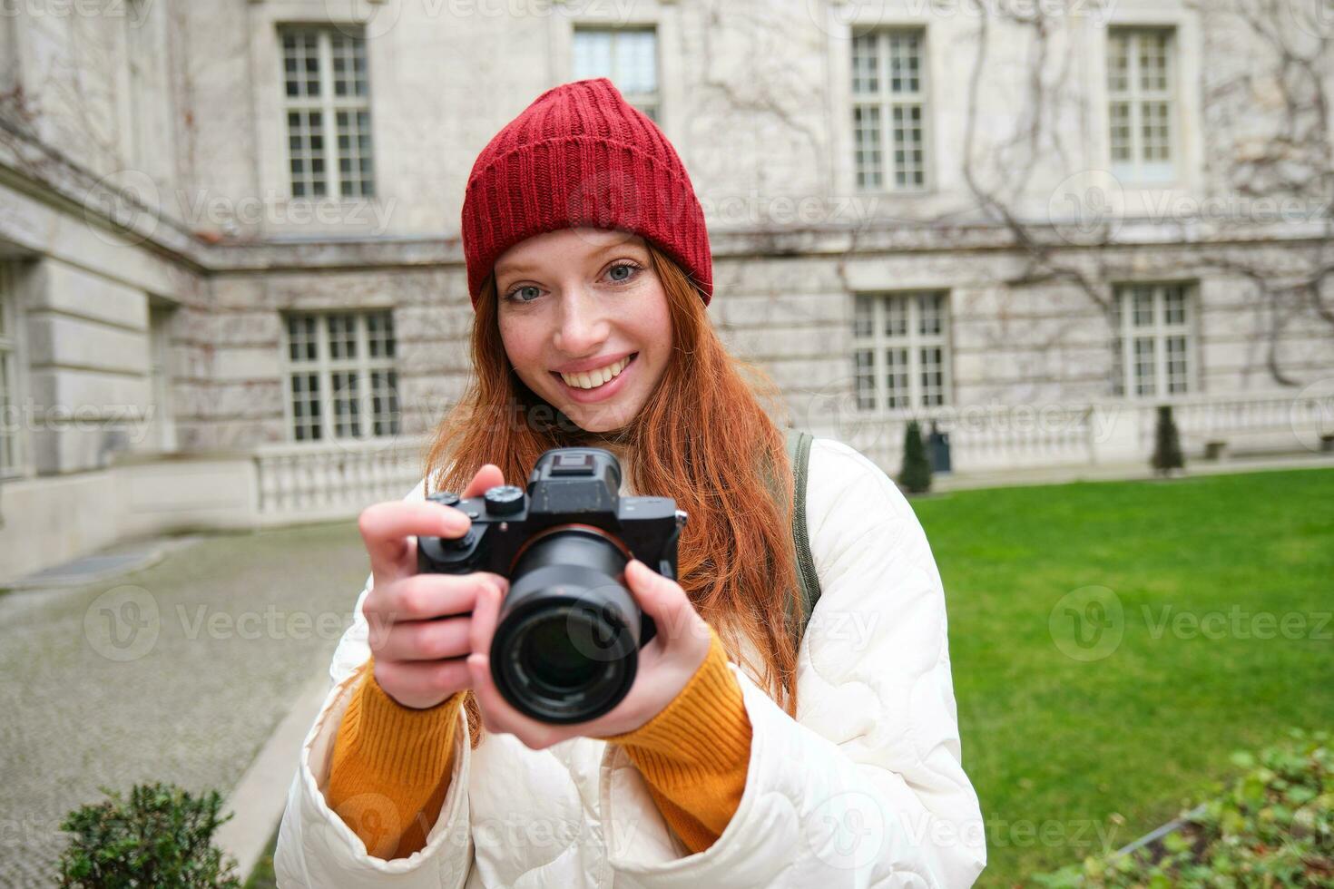 testa Rossa ragazza fotografo prende fotografie su professionale telecamera all'aperto, cattura stile di strada colpi, sembra eccitato mentre assunzione immagini