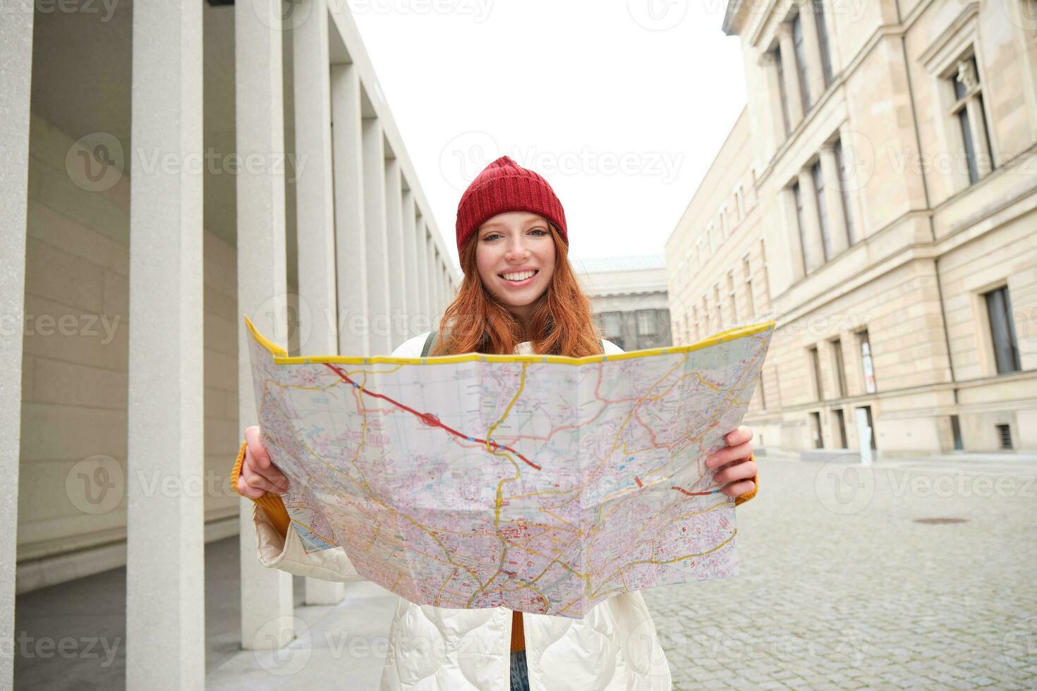 bellissimo testa Rossa donna, turista con città carta geografica, esplora giro turistico storico punto di riferimento, a piedi in giro vecchio cittadina, sorridente felicemente foto