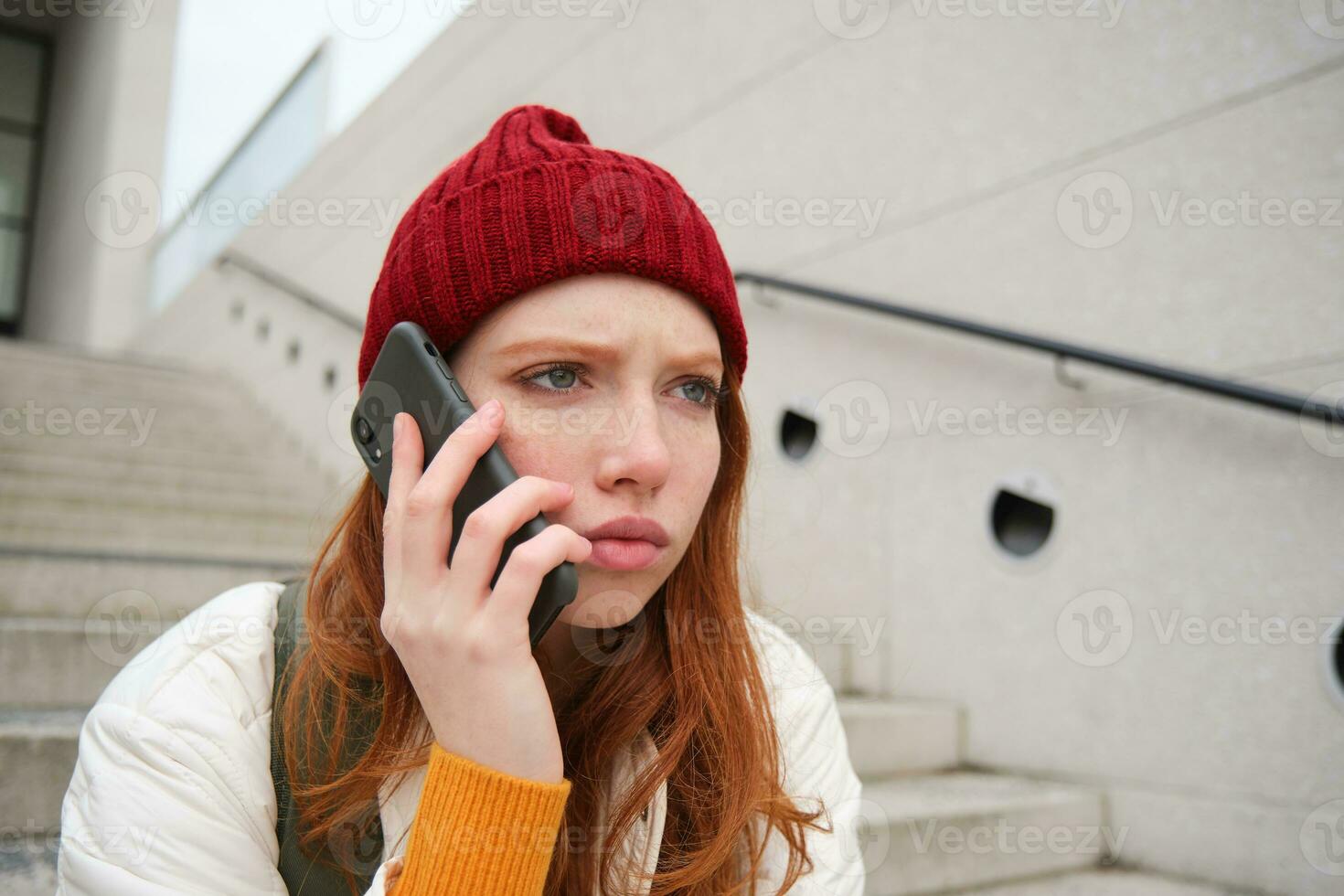 testa Rossa ragazza con ha riguardato viso, guardare preoccupato mentre segreteria Telefono chiamata, sente cattivo notizia al di sopra di telefono conversazione, anelli qualcuno con irritato emozione foto