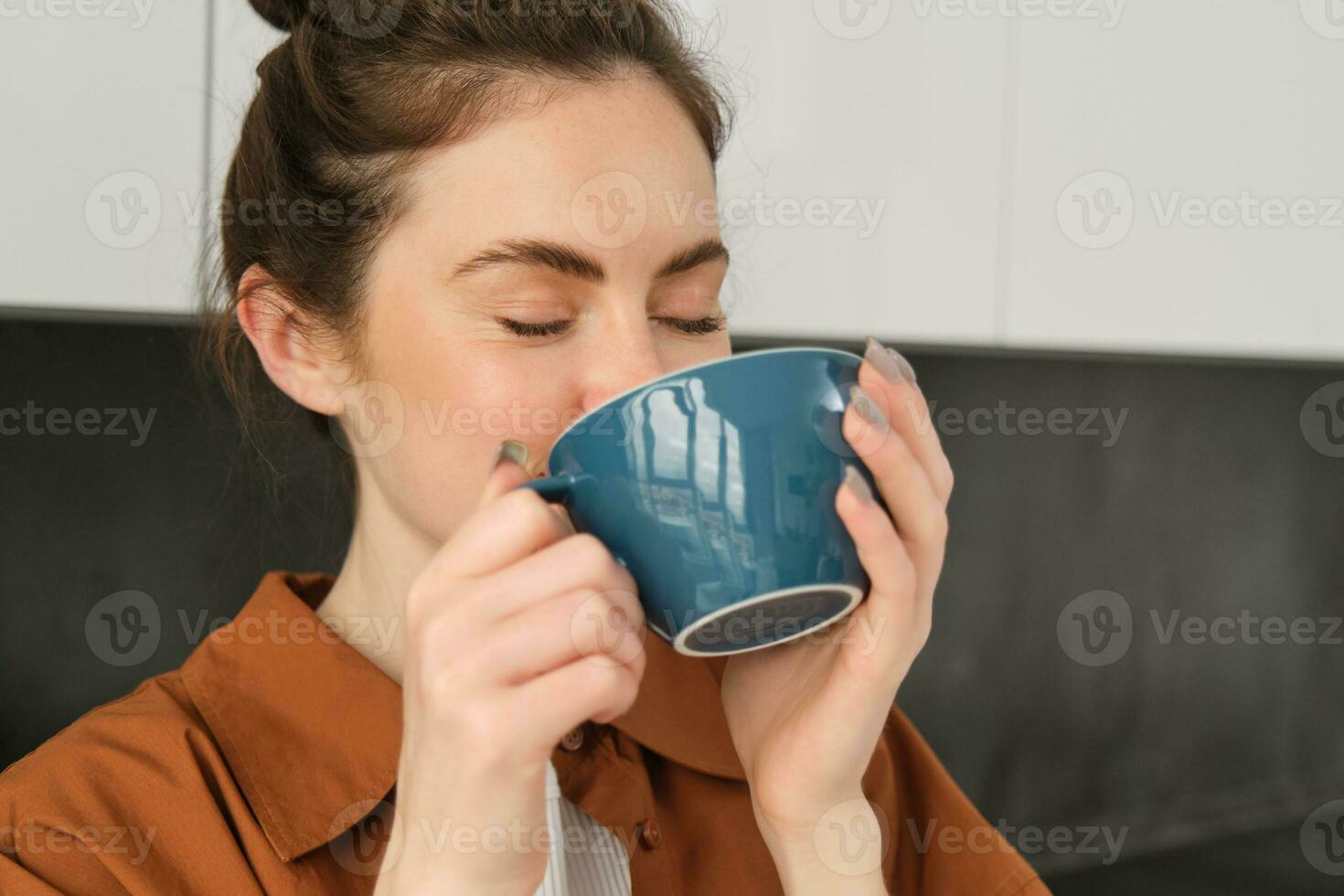 ritratto di bellissimo giovane donna potabile caffè, in piedi nel il cucina con grande tazza, godendo fresco aromatico fagioli, delizioso cappuccino foto