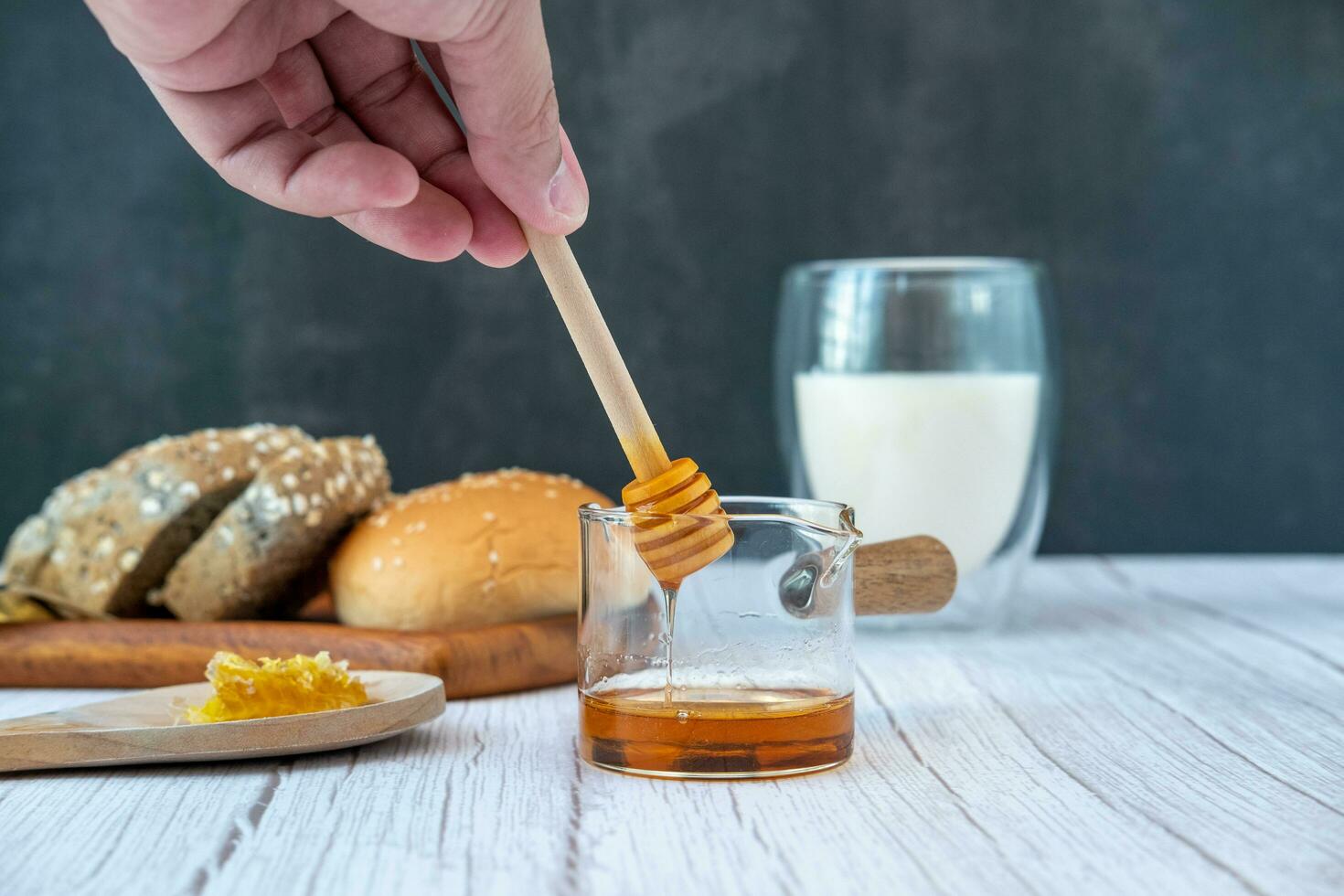 maschio mani siamo utilizzando un' bastone per eccitante miele nel un' misurazione tazza con pane e latte. foto