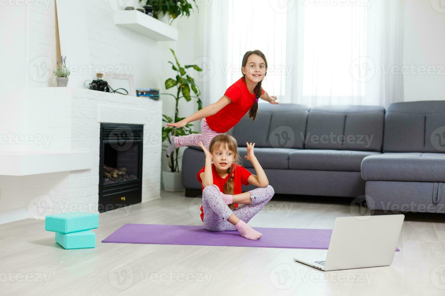 Due poco ragazze praticante yoga, allungamento, fitness di video su taccuino. lontano in linea formazione scolastica addestramento, aerobico a casa. salutare stile di vita, coronavirus, restare casa. bambini sport casa quarantena. foto