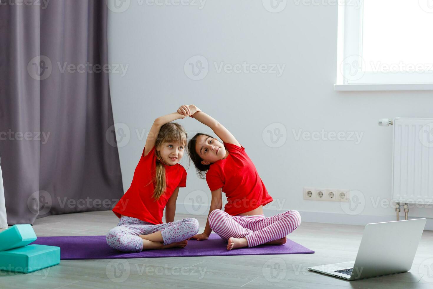 Due poco ragazze praticante yoga, allungamento, fitness di video su taccuino. lontano in linea formazione scolastica addestramento, aerobico a casa. salutare stile di vita, coronavirus, restare casa. bambini sport casa quarantena. foto