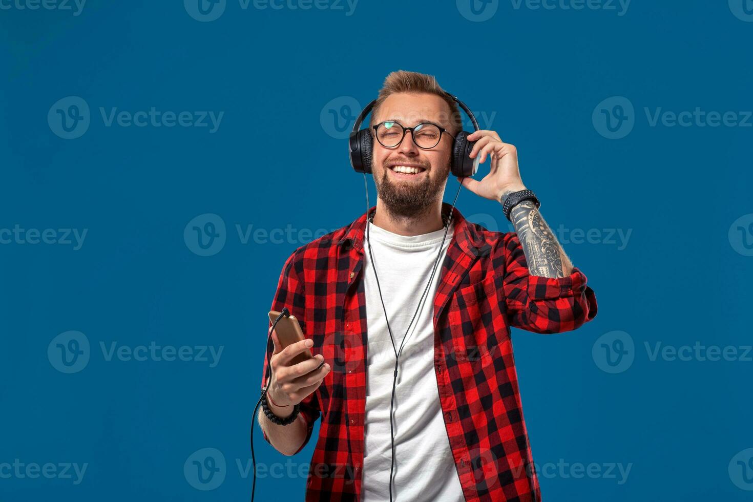 contento giovane uomo ascoltando per musica con cuffia. bello sorridente tipo nel scacchi camicia con chiuso occhi danza con cuffia. foto