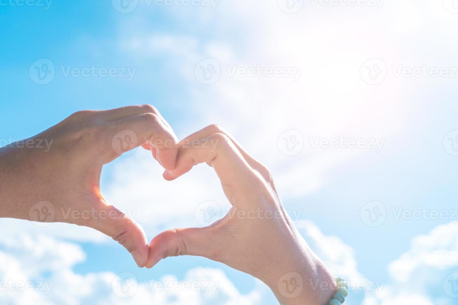 la mano della donna fa la forma del cuore su cielo blu e sulla spiaggia. foto