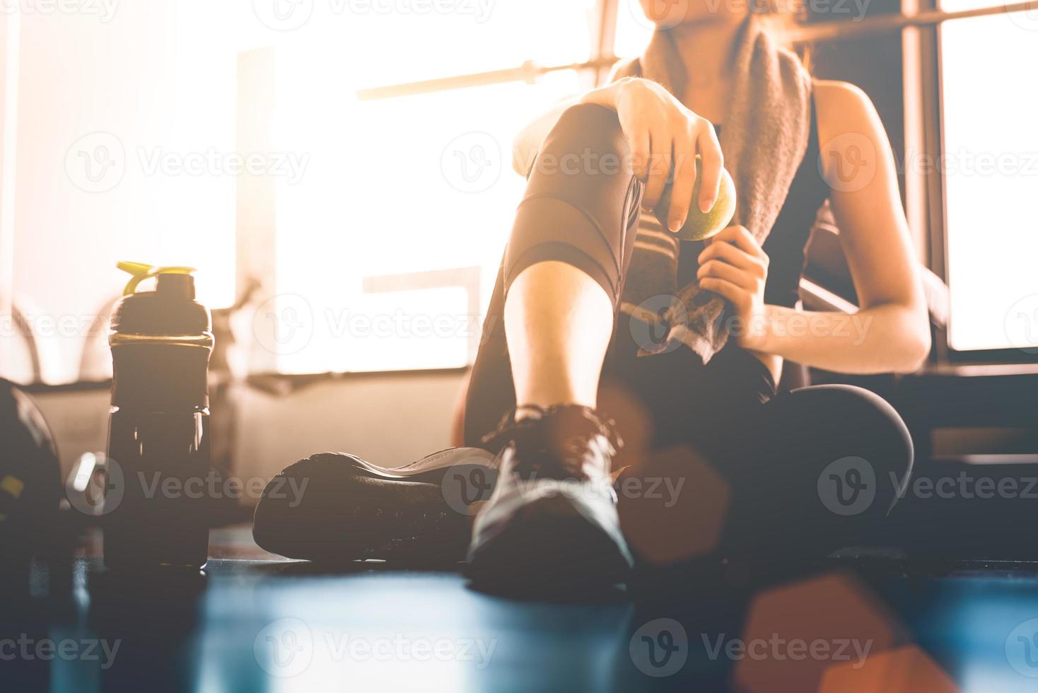 donna sportiva seduta e riposata dopo l'allenamento o l'esercizio in palestra con frullato proteico o acqua potabile sul pavimento. concetto di relax. tema di allenamento per la forza e body build. tono caldo e freddo foto