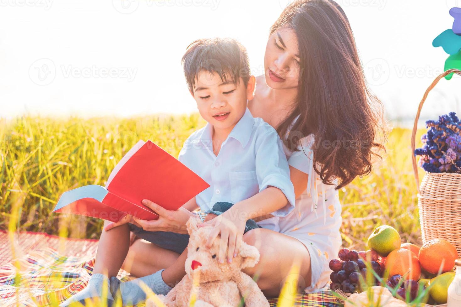 piccolo ragazzo asiatico e sua madre che leggono libri quando fanno picnic nel prato. madre e figlio che imparano insieme. festeggiando la festa della mamma e apprezzando il concetto. persone estive ed educazione allo stile di vita foto