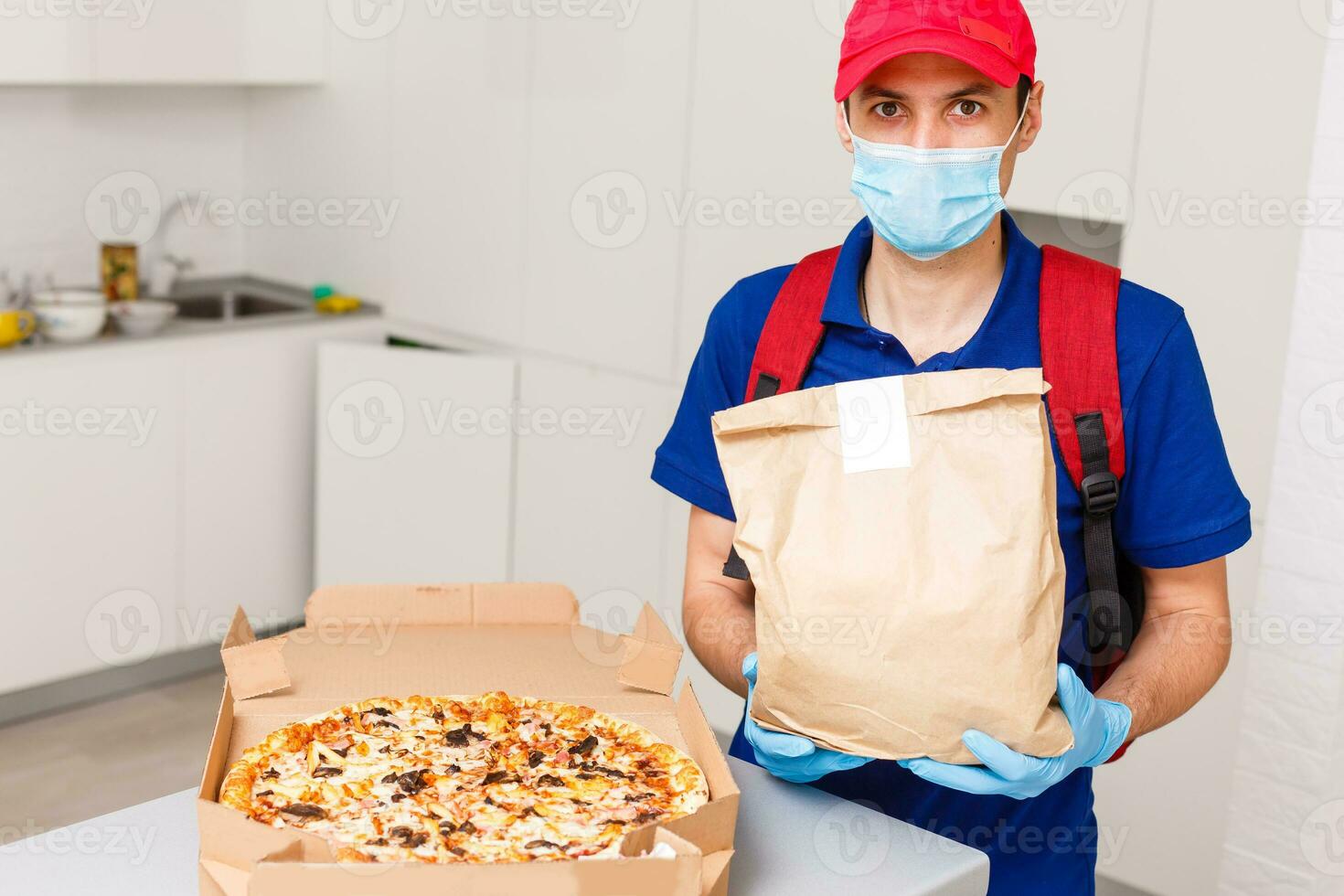 consegna uomo dipendente nel rosso berretto maglietta uniforme maschera guanti dare cibo ordine Pizza scatole isolato su giallo sfondo studio. servizio quarantena pandemia coronavirus virus influenza 2019-ncov concetto foto