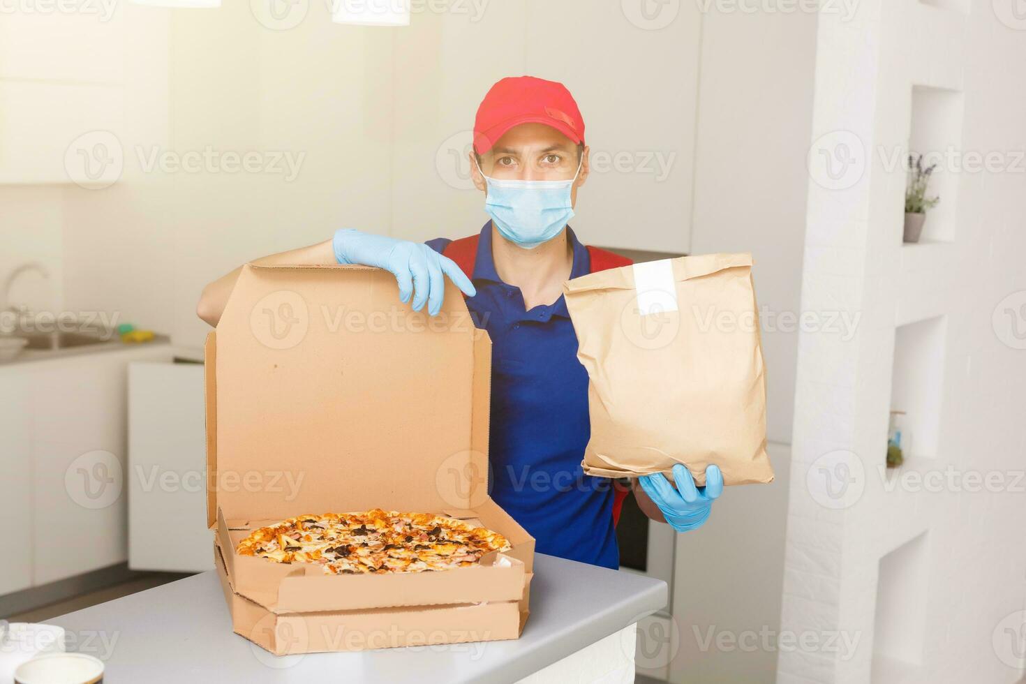 consegna uomo dipendente nel rosso berretto maglietta uniforme maschera guanti dare cibo ordine Pizza scatole isolato su giallo sfondo studio. servizio quarantena pandemia coronavirus virus influenza 2019-ncov concetto foto