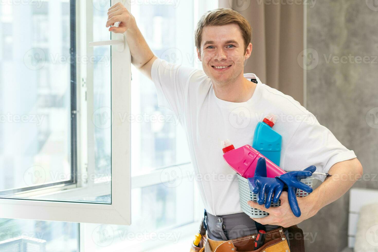 lato Visualizza di sorridente uomo con bottiglia di detergente e straccio pulizia finestra a casa foto