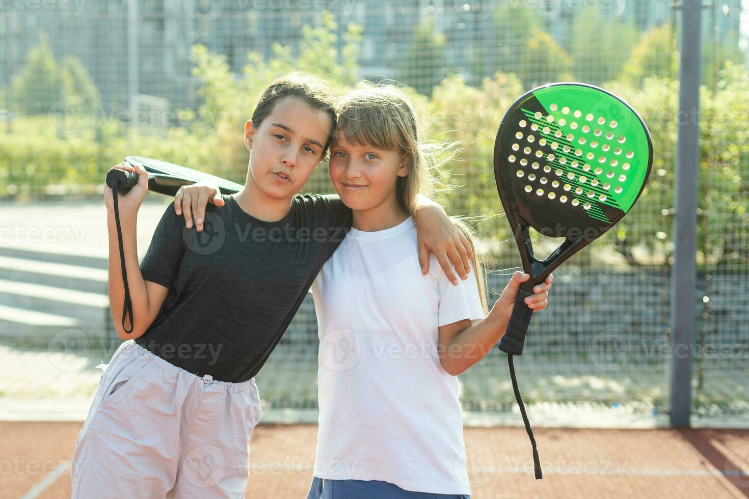 adolescenziale ragazze con racchette e palle in piedi nel padel Tribunale, guardare a telecamera e sorridente. foto