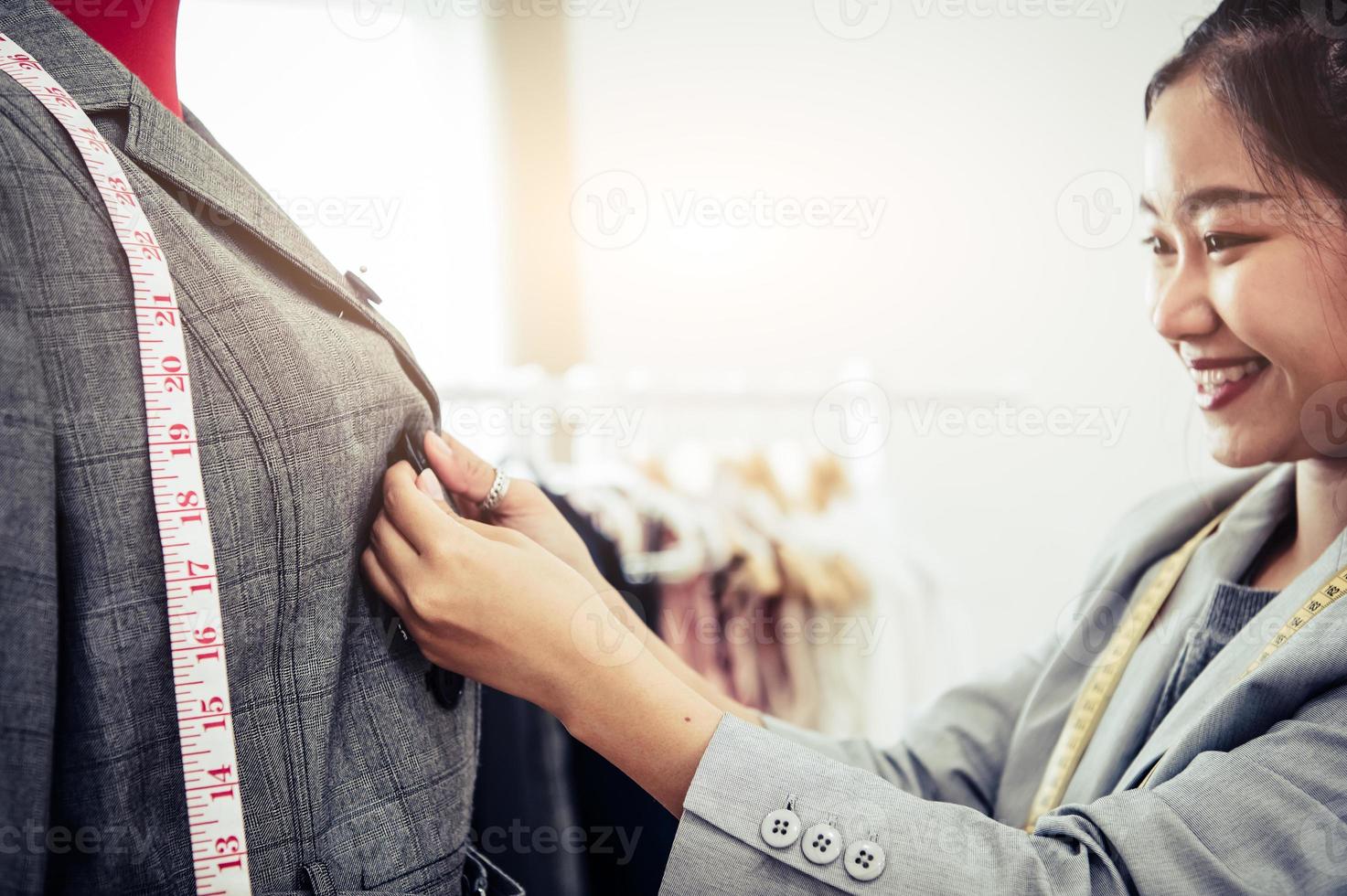 ragazza asiatica dello stilista femminile che si adatta ai vestiti dell'uniforme del vestito convenzionale sul modello del manichino. showroom alla moda dello stilista. concetto di cucito e sarto. stilista sarto creativo foto