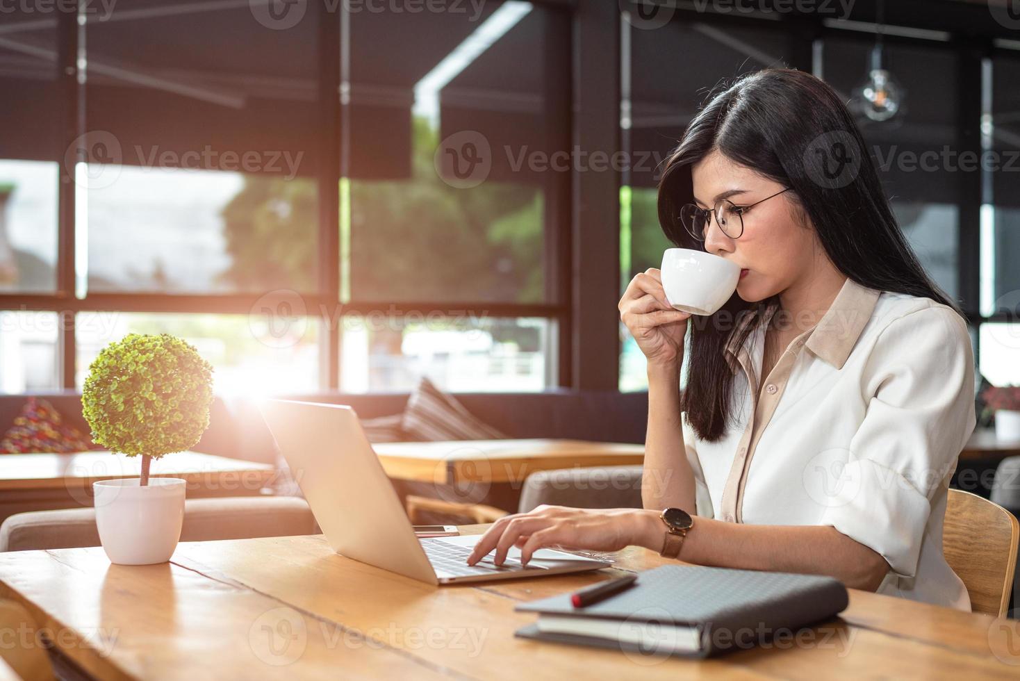 donna lavoratrice asiatica che utilizza laptop e beve caffè nella caffetteria. concetto di persone e stili di vita. tecnologia e tema aziendale. tema freelance e occupazione. maniaco del lavoro nel concetto notturno foto