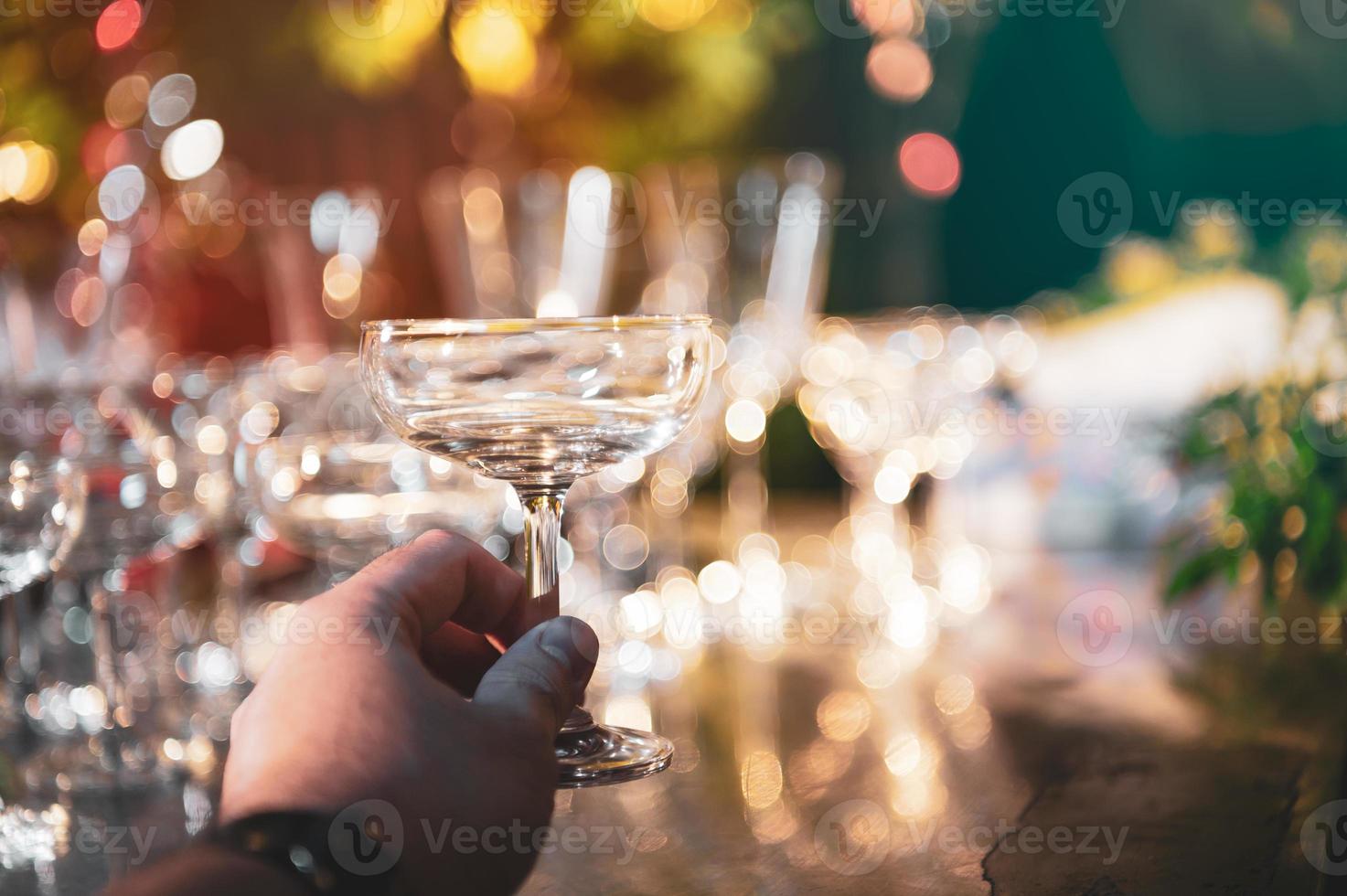 Primo piano mano azienda martini bicchieri di vino sul bancone all'aperto bar in giardino di notte per la celebrazione party foto