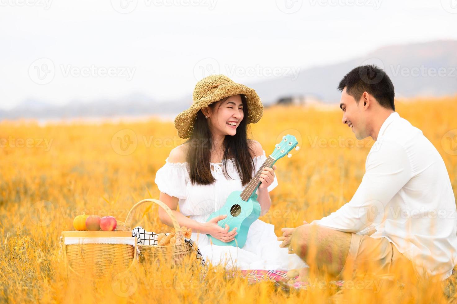 due giovani coppie asiatiche in un prato autunnale che fanno picnic in viaggio di nozze in abiti bianchi, chitarra ukulele e cesto di frutta. stile di vita delle persone e concetto di matrimonio. natura e concetto di giorno di viaggio foto