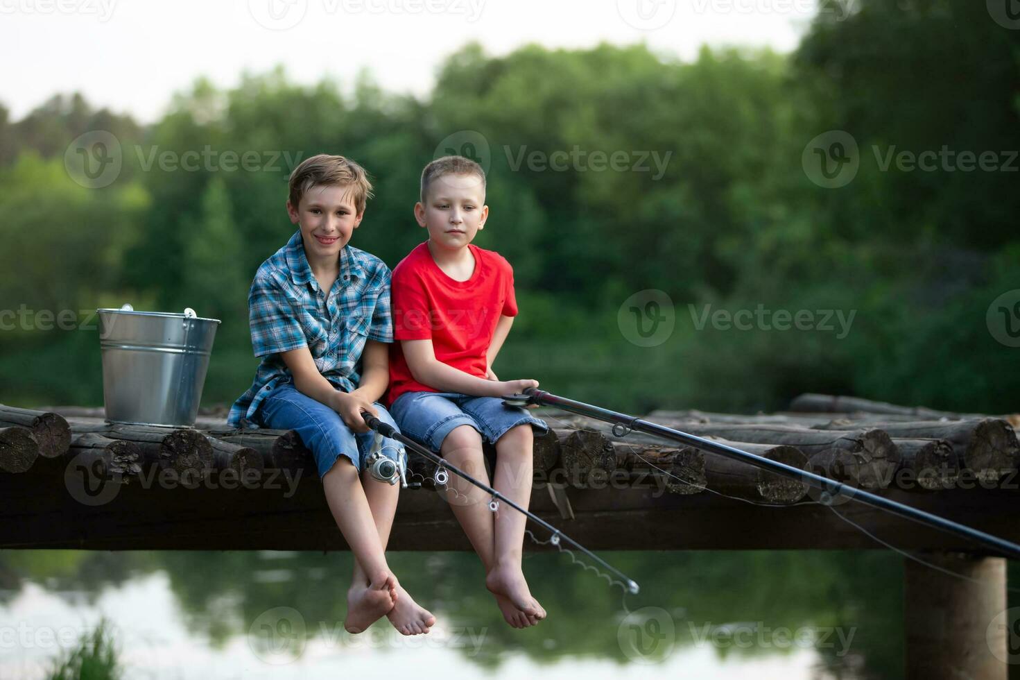 Due ragazzi sedersi con pesca canne su un' di legno ponte e pesce su il lago. foto