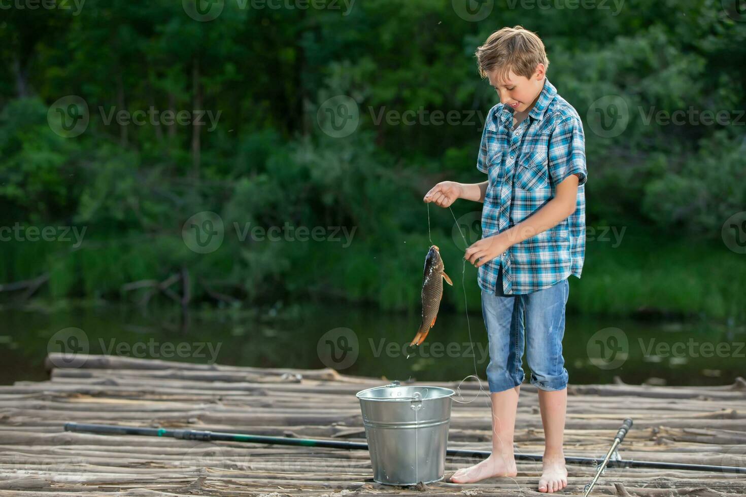 un' pescatore ragazzo sta su un' di legno ponte e sembra a il catturato carpa. foto