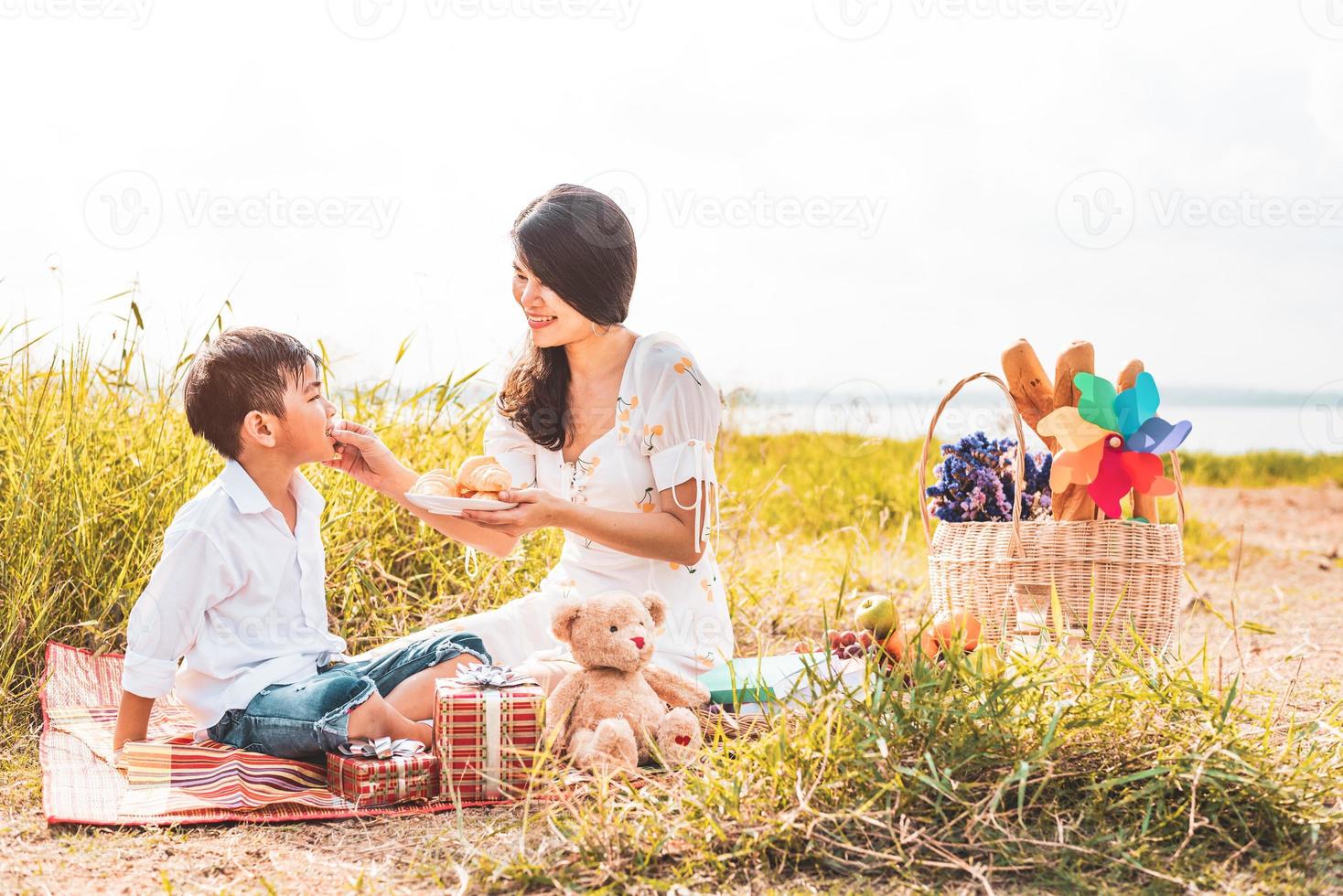 bella mamma asiatica che alimenta uno spuntino a suo figlio nel prato quando fa un picnic. madre e figlio che giocano insieme. festeggiando la festa della mamma e apprezzando il concetto. persone estive e tema stile di vita foto