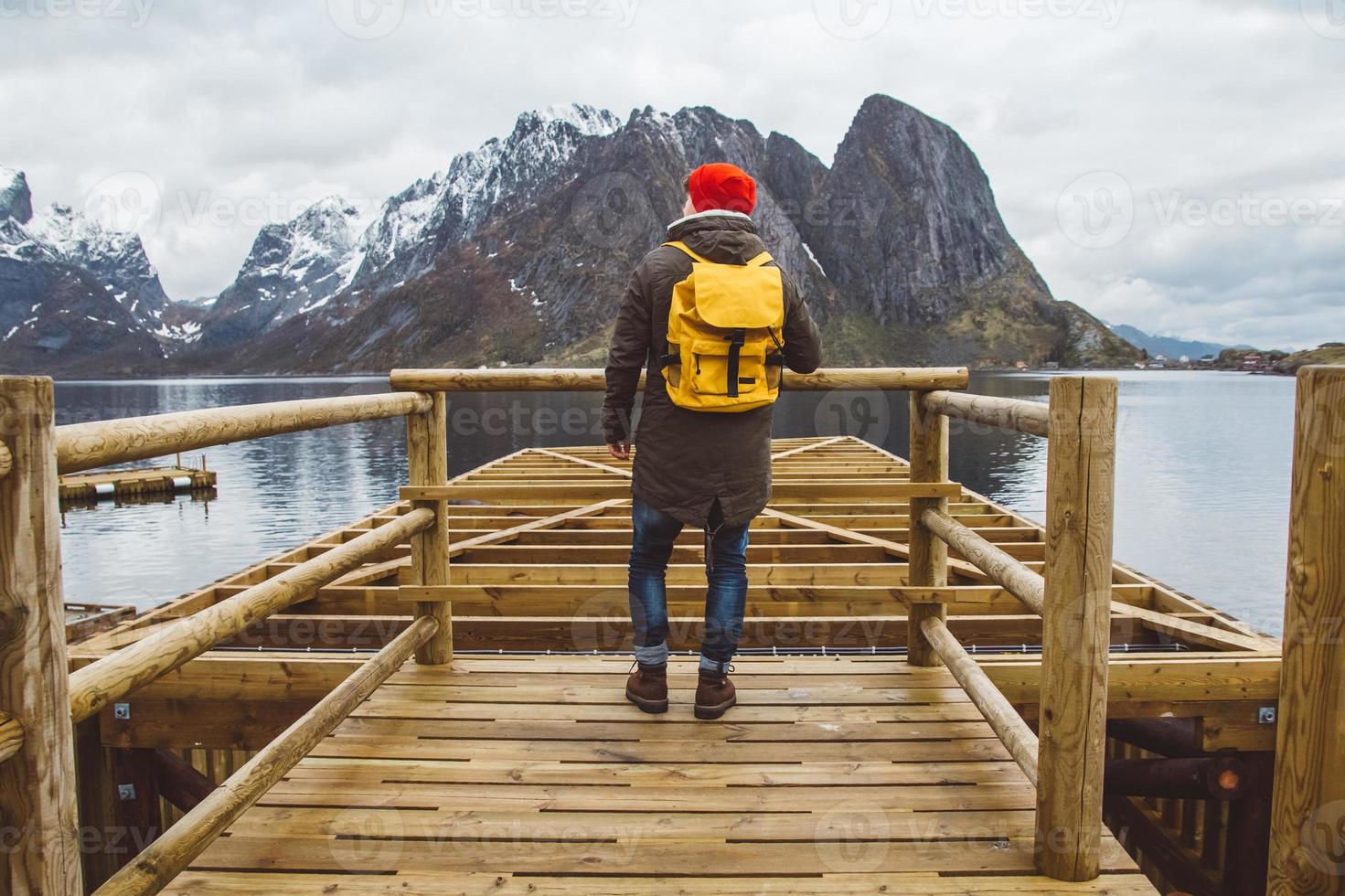 uomo viaggiatore con uno zaino in piedi sul molo di legno sullo sfondo della montagna e del lago foto