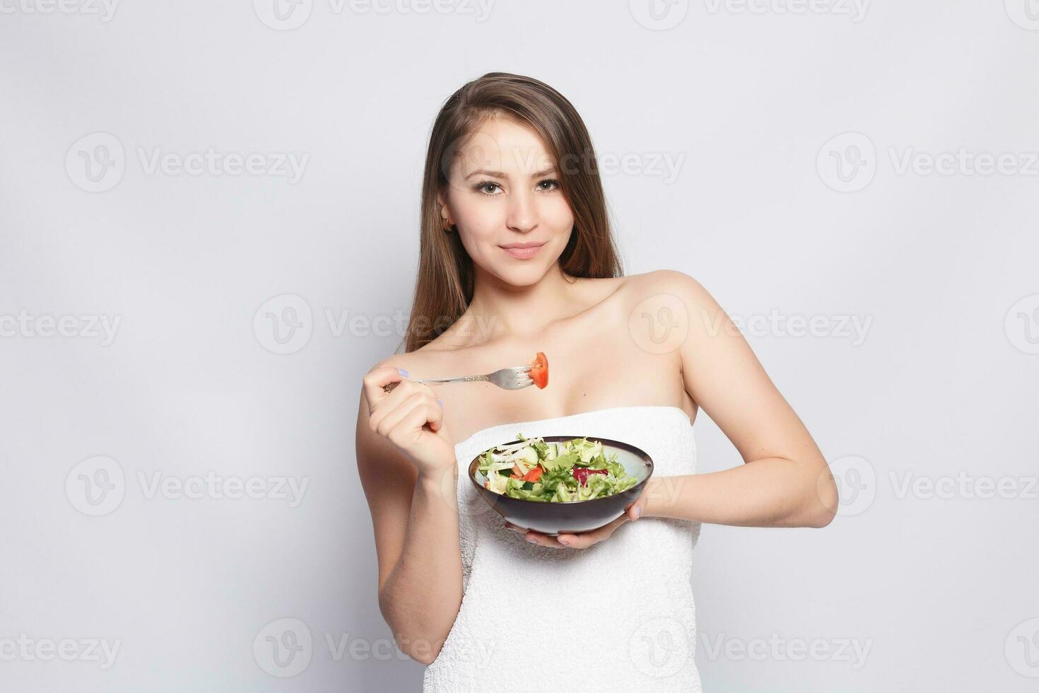 bellissimo brunetta ragazza nel asciugamano mangiare fresco insalata e sorridente foto