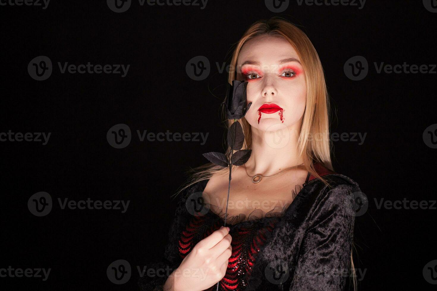 bellissimo biondo vampiro donna con un' rosa al di sopra di nero sfondo per Halloween. foto