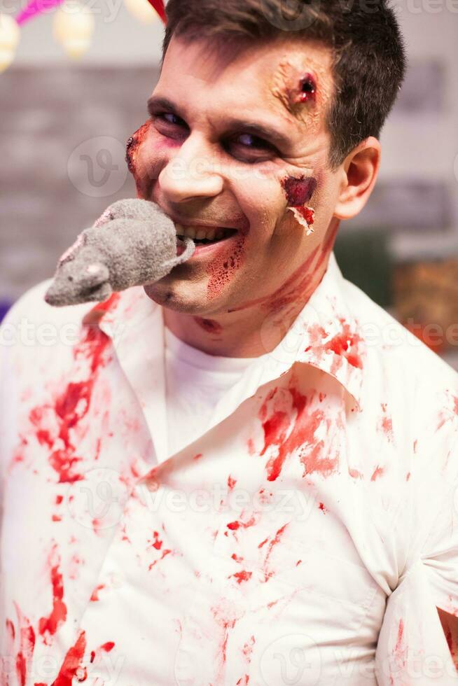 uomo vestito su piace un' sanguinoso zombie con un' ratto nel il suo bocca a Halloween celebrazione. foto