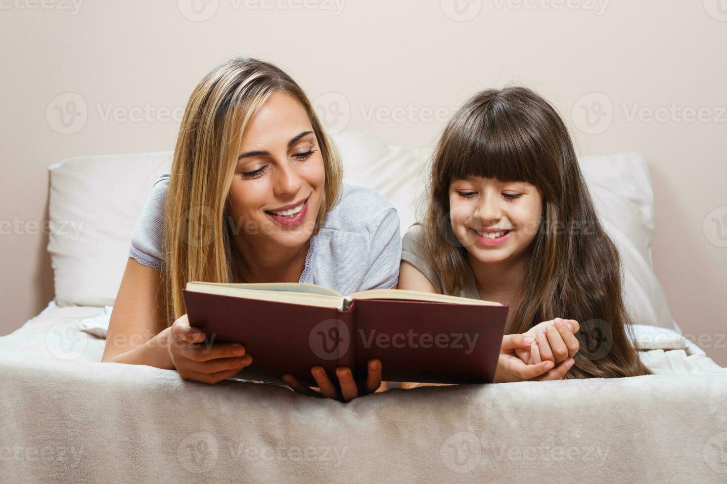 madre e figlia che leggono insieme libro a letto foto