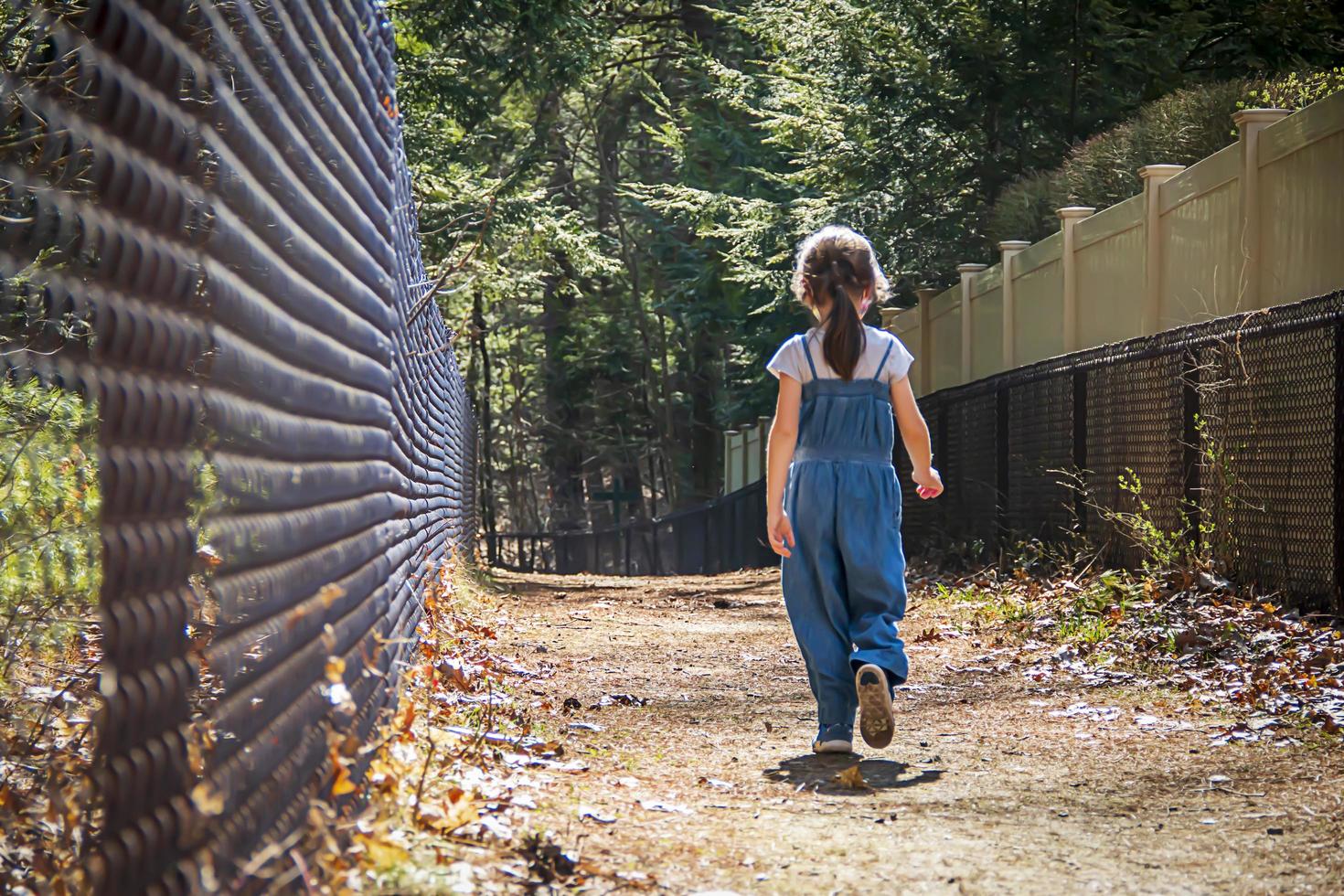 bambino che cammina lungo un sentiero oltre un recinto nero foto