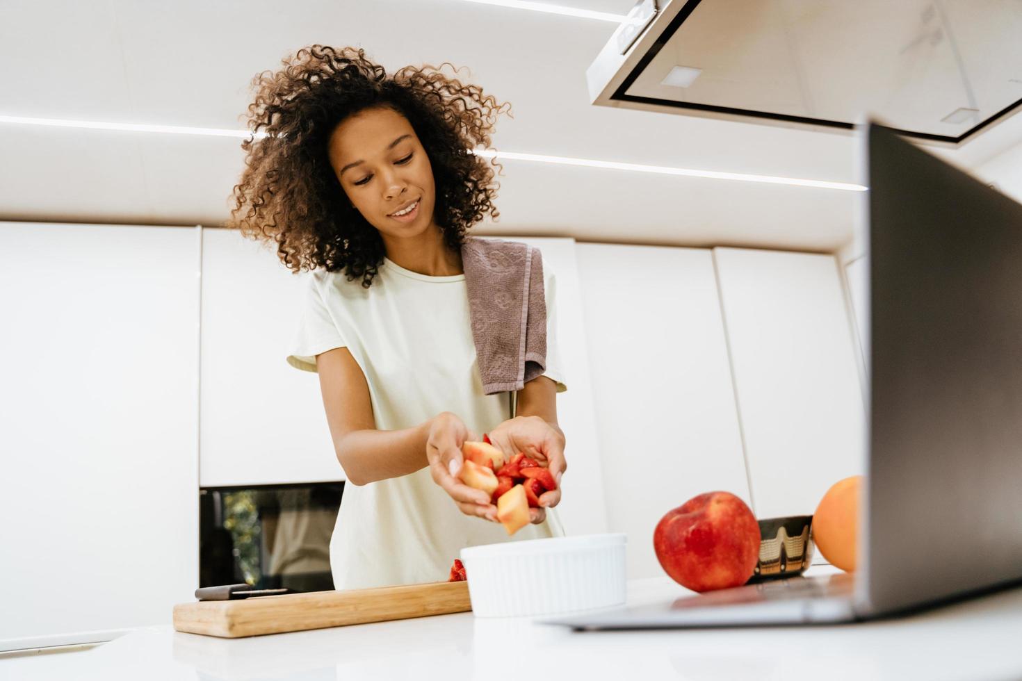 giovane donna nera che prepara insalata mentre usa il computer portatile in cucina foto