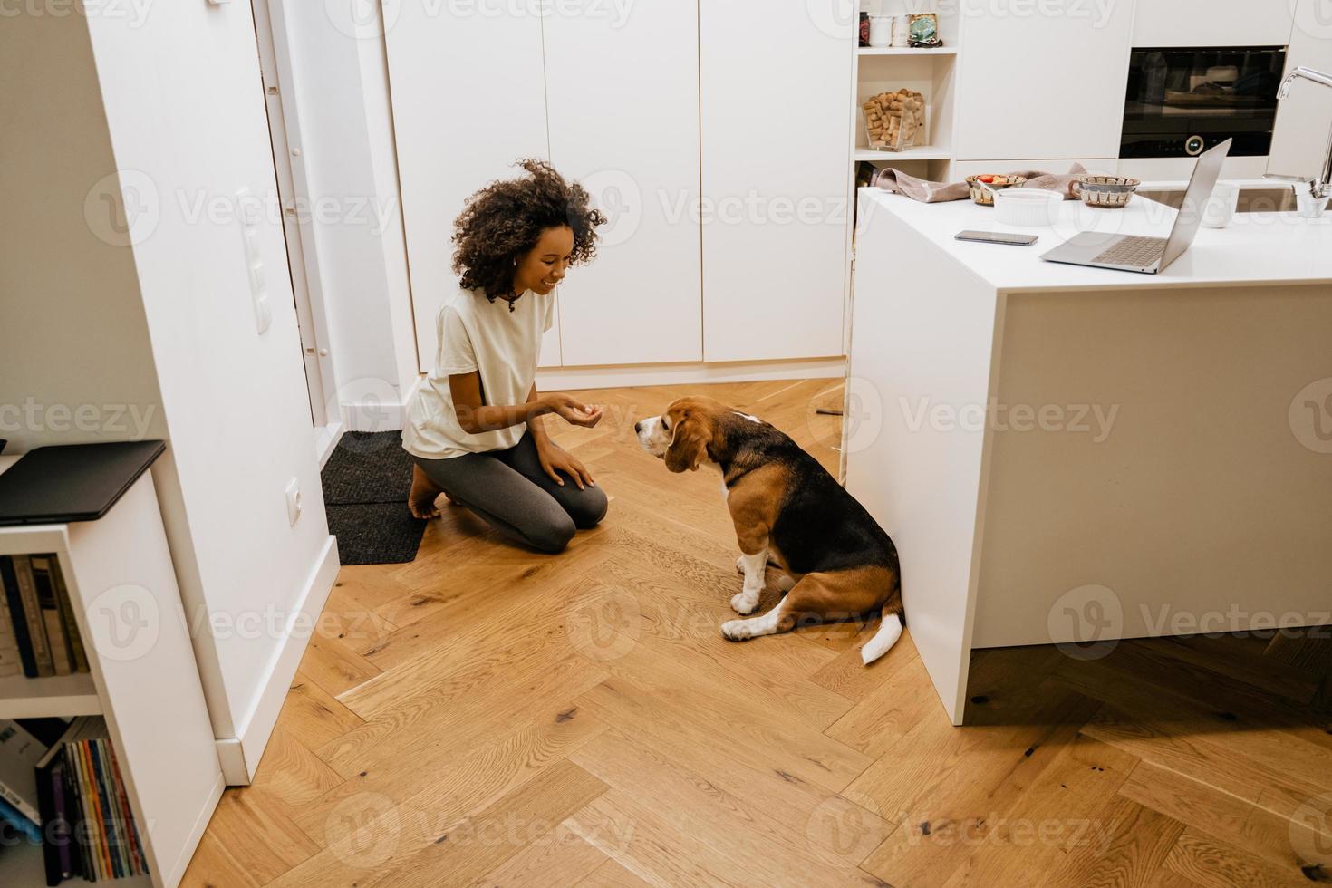 giovane donna nera con gli auricolari che sorride mentre dà da mangiare al suo cane foto