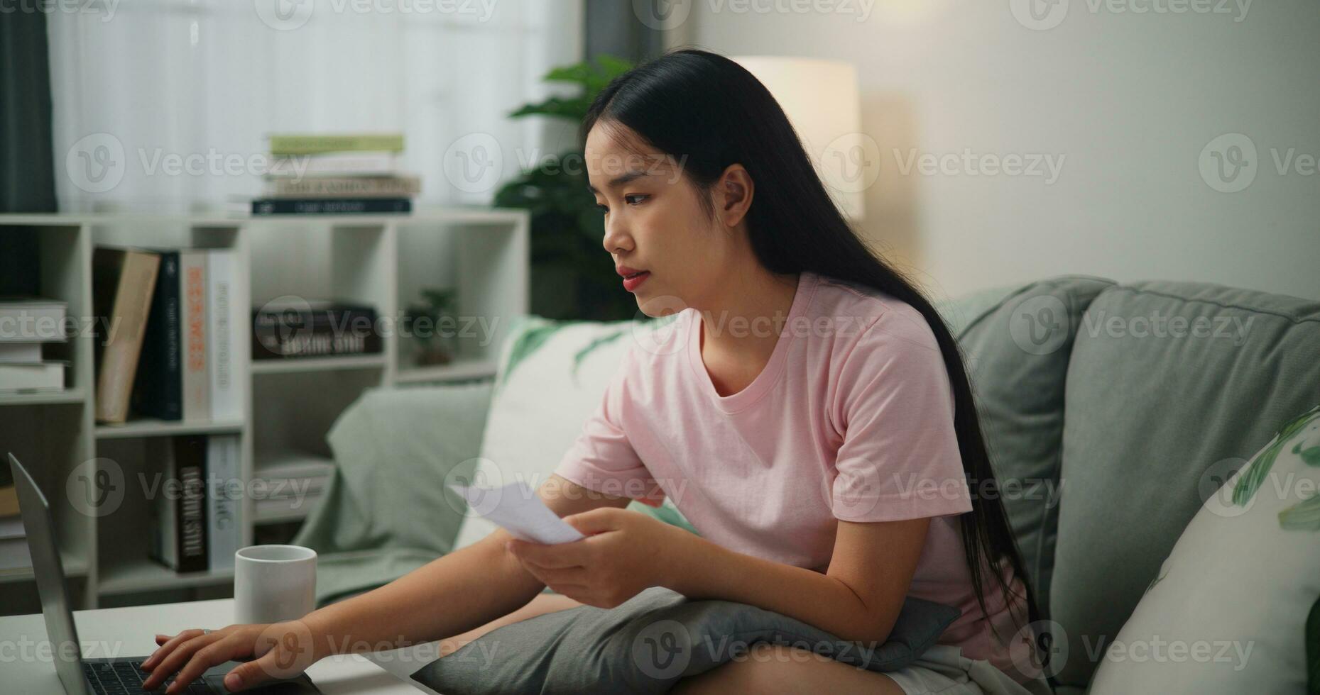 ritratto di giovane asiatico donna guardare a il computer portatile schermo Tenere fattura ricevuta nel mano pianificazione famiglia bilancio confrontando carta e in linea documento,casa finanza foto