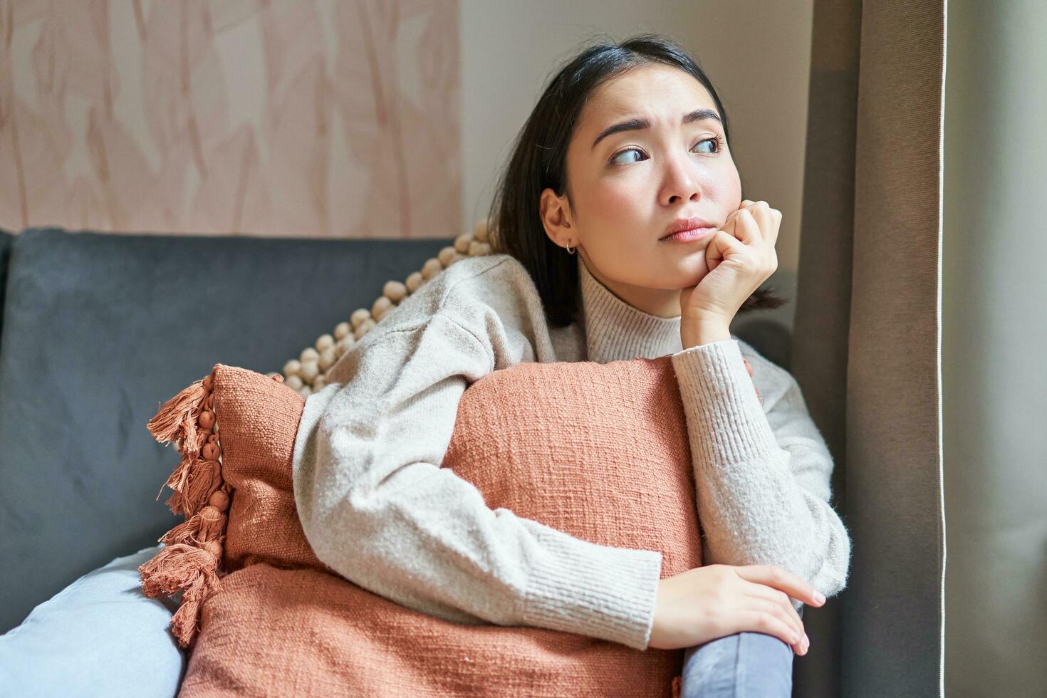 donne e benessere concetto. ritratto di riflessivo asiatico donna seduta su divano con cuscino, guardare a parte con pensiero concentrato viso foto