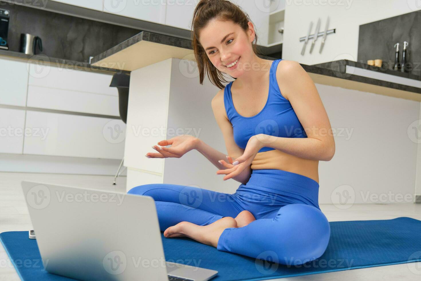 ritratto di in forma e sano, femmina fitness istruttore seduta su pavimento a casa, parlando per computer portatile, insegnamento in linea classe yoga o allenarsi formazione foto