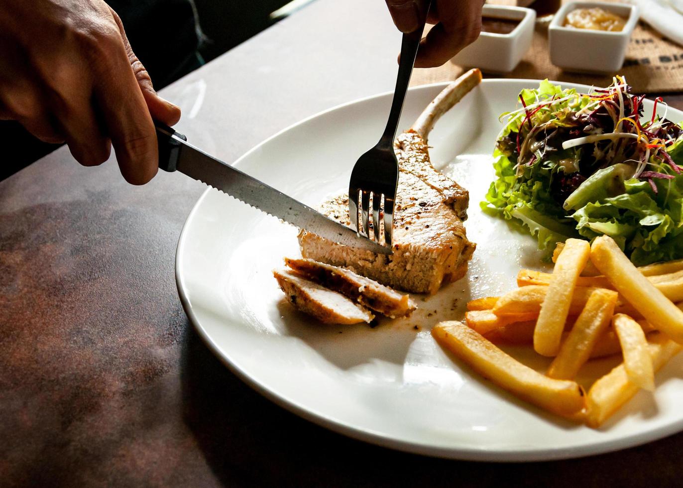 taglio coltello braciole di maiale alla griglia bistecca da vicino, bistecca di braciola di maiale con insalata e patatine fritte foto