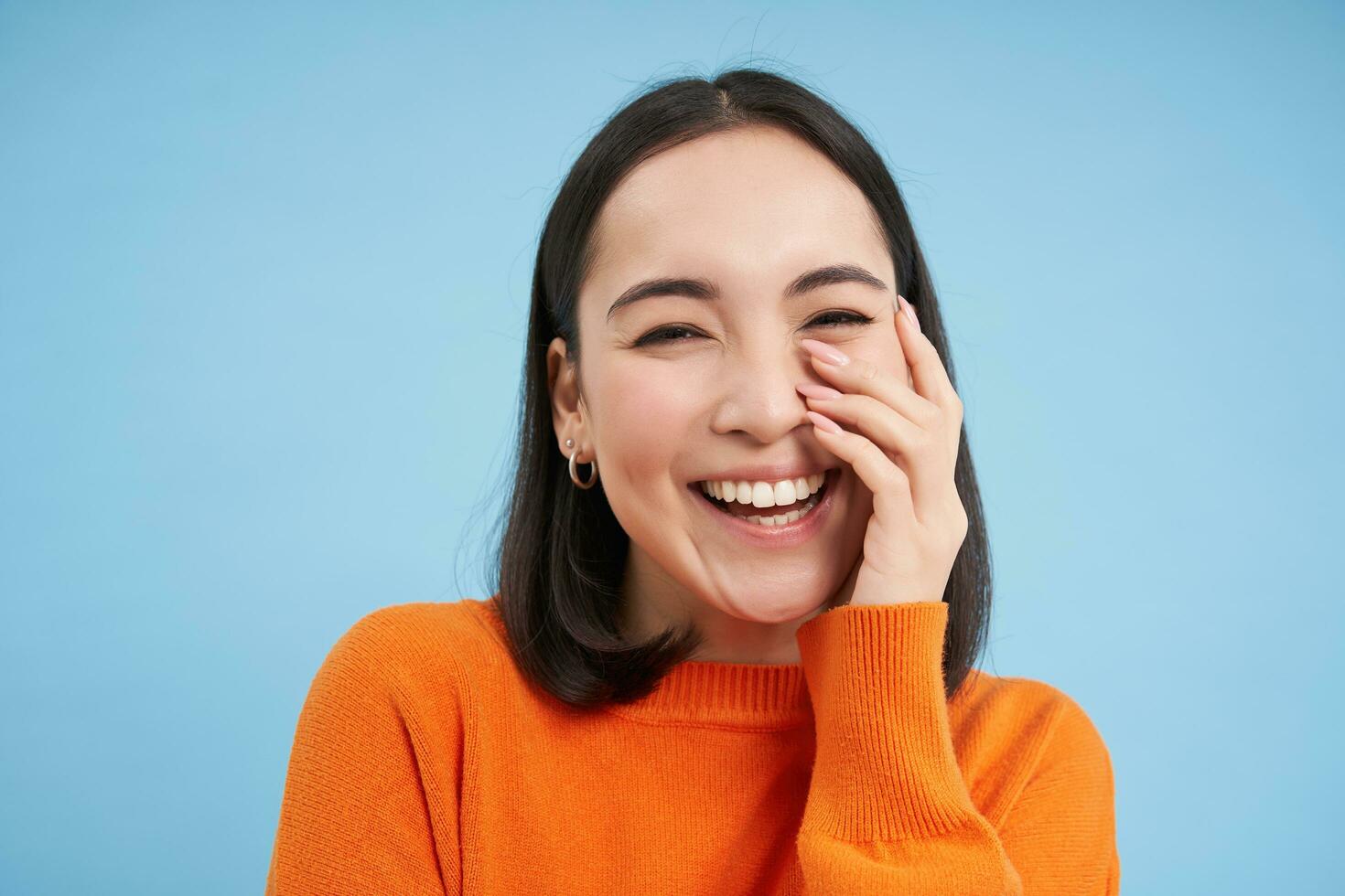 contento coreano donna ridendo e sorridente, esprime Candido emozioni di la gioia, in piedi al di sopra di blu sfondo foto