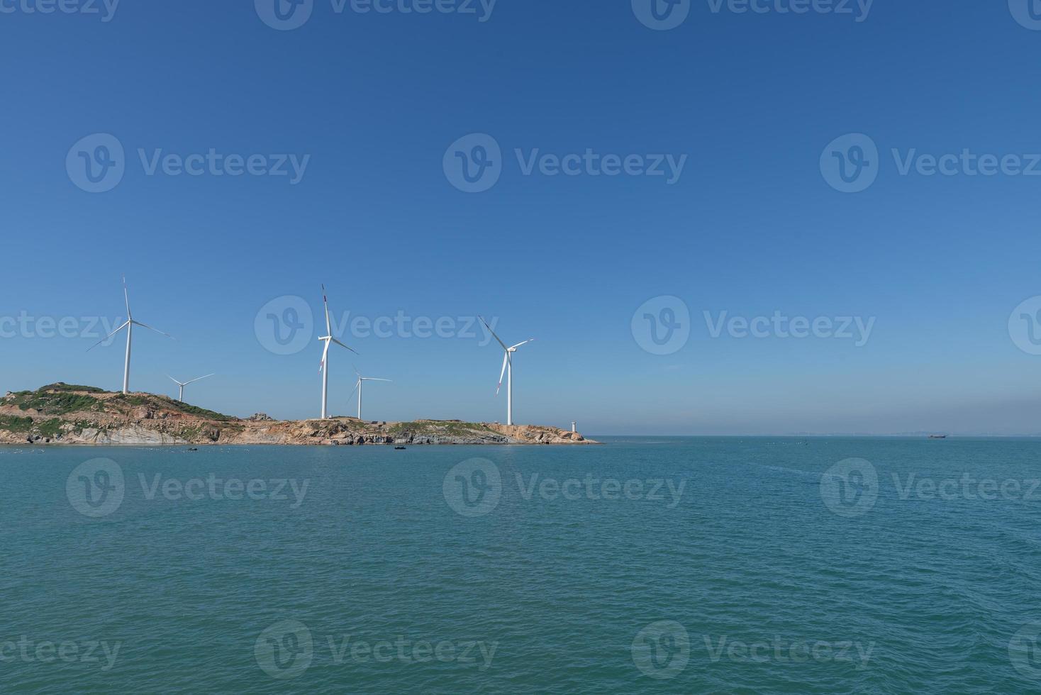 sull'isola in mezzo al mare, molte pale eoliche sono installate sotto il cielo azzurro foto