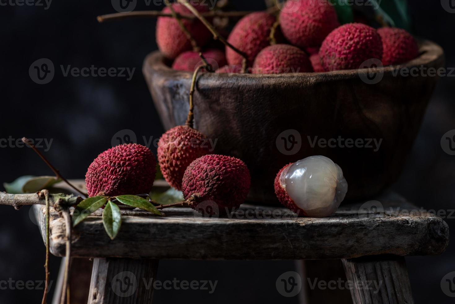 il litchi è posto in un piatto di legno, sbucciato o non aperto, su un tavolo con venature di legno scuro foto