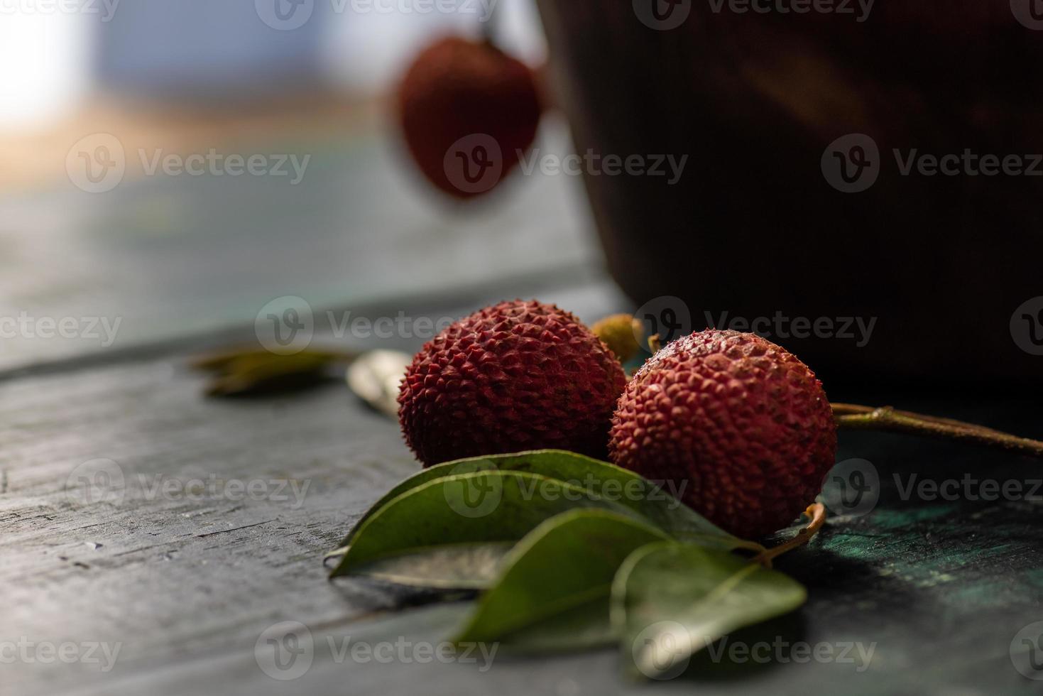 il litchi è posto in un piatto di legno, sbucciato o non aperto, su un tavolo con venature di legno scuro foto