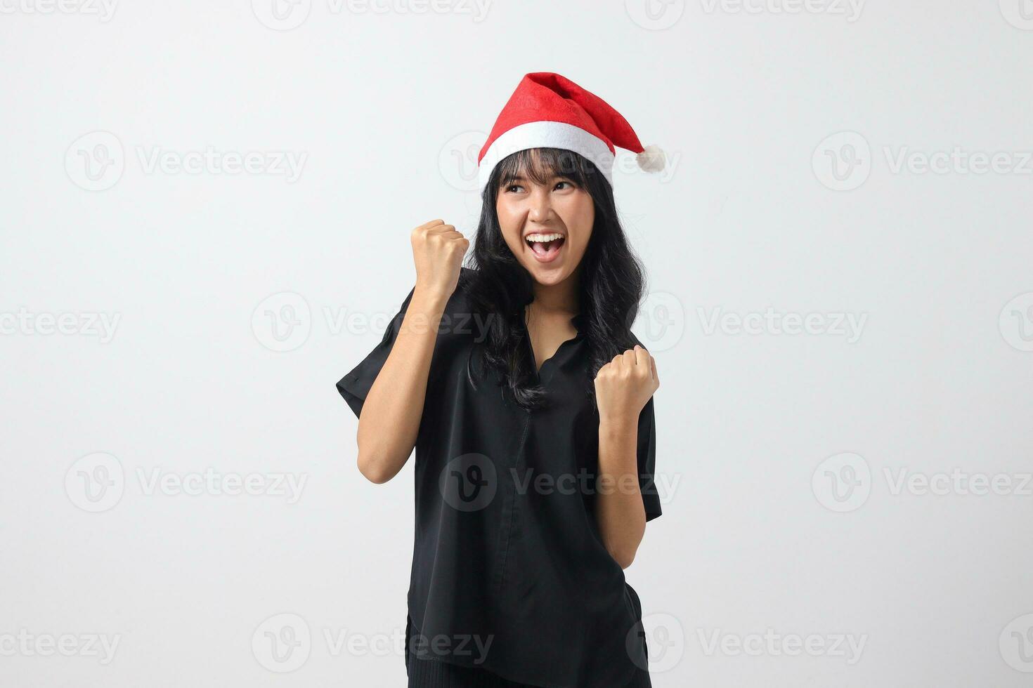 ritratto di eccitato asiatico donna con rosso Santa cappello raccolta cazzotto, festeggiare successo. nuovo anno e Natale concetto. isolato Immagine su bianca sfondo foto