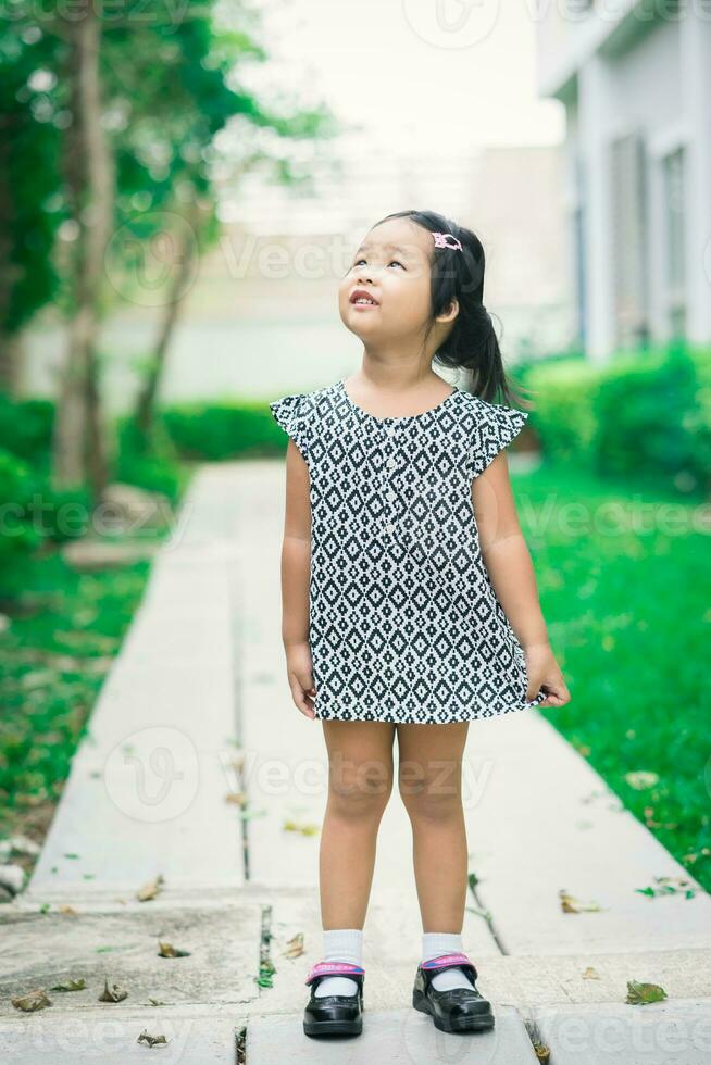 ritratto di felice bambina asiatica in abito in piedi sul sentiero nel parco foto