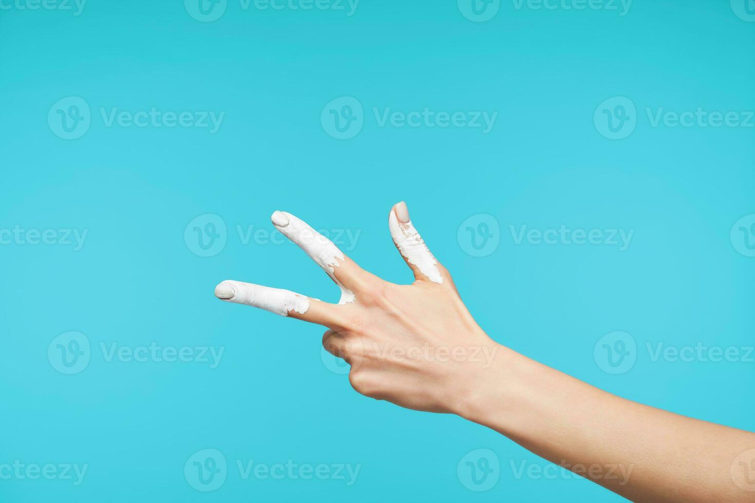 orizzontale tiro di dipinto della signora mano essere sollevato mentre mostrando figura tre nel corpo linguaggio o pace cartello, in posa contro blu sfondo foto
