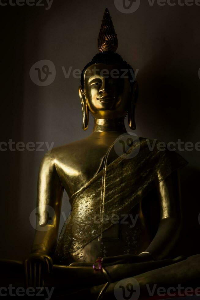 un' statua di oro Budda con ombra su parete nel il buio camera foto