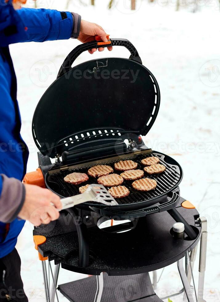 uomo grigliate bistecche su un' portatile barbecue, nevoso inverno barbecue foto