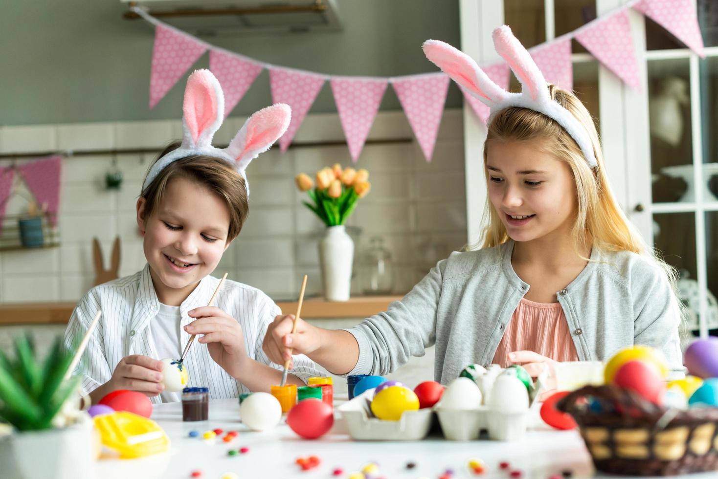 due bambini felici in orecchie da coniglio dipingono le uova di pasqua al tavolo. foto